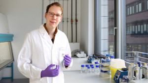 Das Bild zeigt Dr. Christopher Nelke im Labor. In den Händen hält er eine Probe. The picture shows Dr Christopher Nelke in the laboratory. He is holding a sample in his hands.