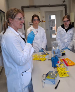 Dr. Christina Sengstock erklärt ihrer Gruppe das Experiment zum Ausplattieren.  Drei Teilnehmerinnen hören aufmerksam zu.