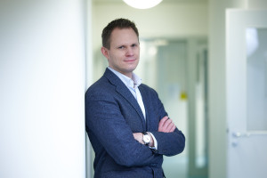 Das Bild zeigt Prof. Dr. Mirko Trilling mit verschränkten Armen, an einer Wand lehnend. The picture shows Prof Dr Mirko Trilling with his arms folded, leaning against a wall.