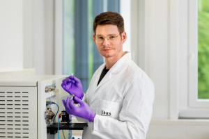 Daniel Foest steht im Labor und hält ein Papier mit einer Leberprobe, die er am Massenspektrometer untersucht.